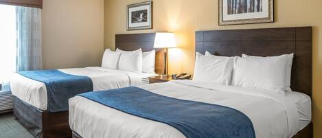 A hotel room with two beds, a nightstand with a lamp, and two framed pictures on the wall.