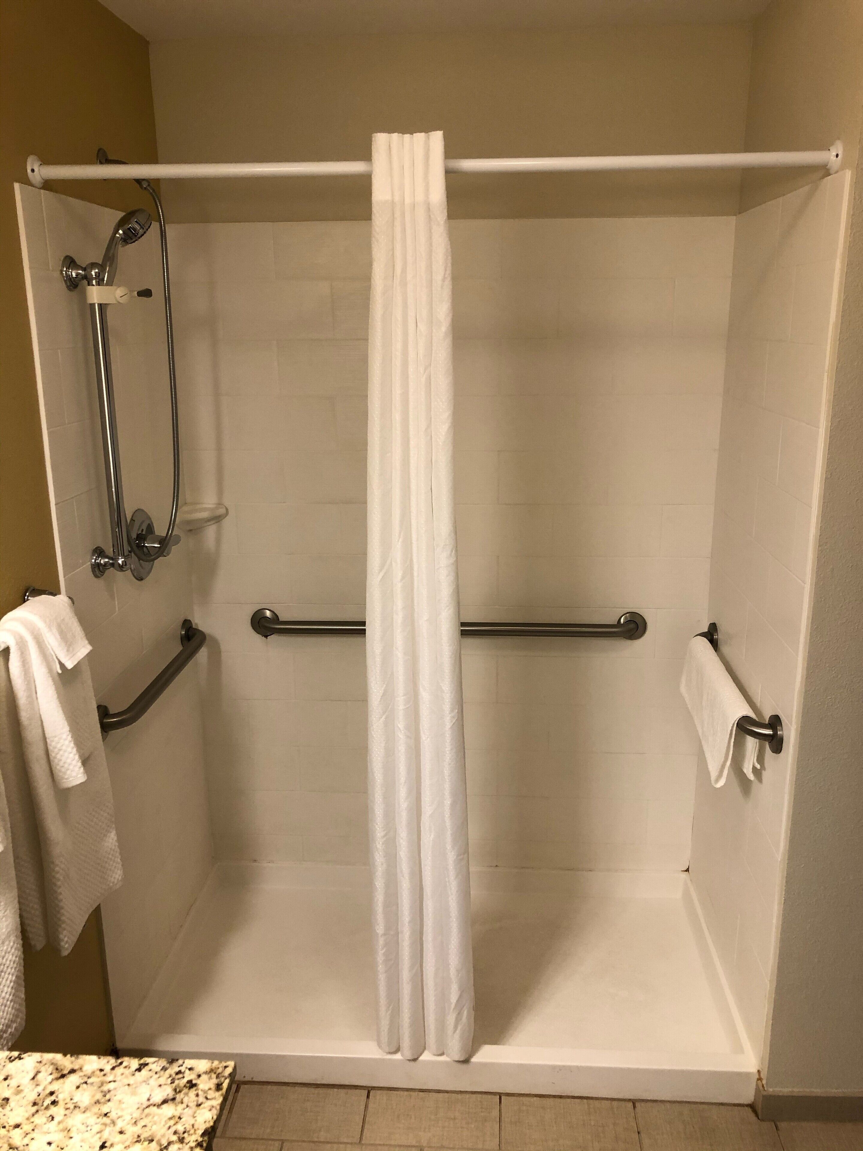 A shower with a white curtain, grab bars, and a towel rack.