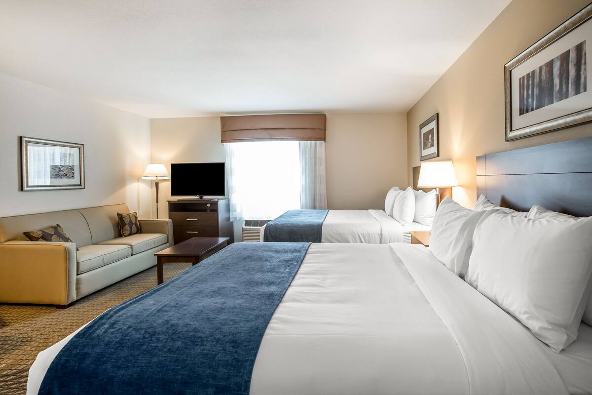 Een hotelkamer met twee bedden, een bank, een televisie en een bureau.