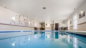 Piscina interna com água cristalina, parede revestida com padrão floral e placa de aviso de salva-vidas.