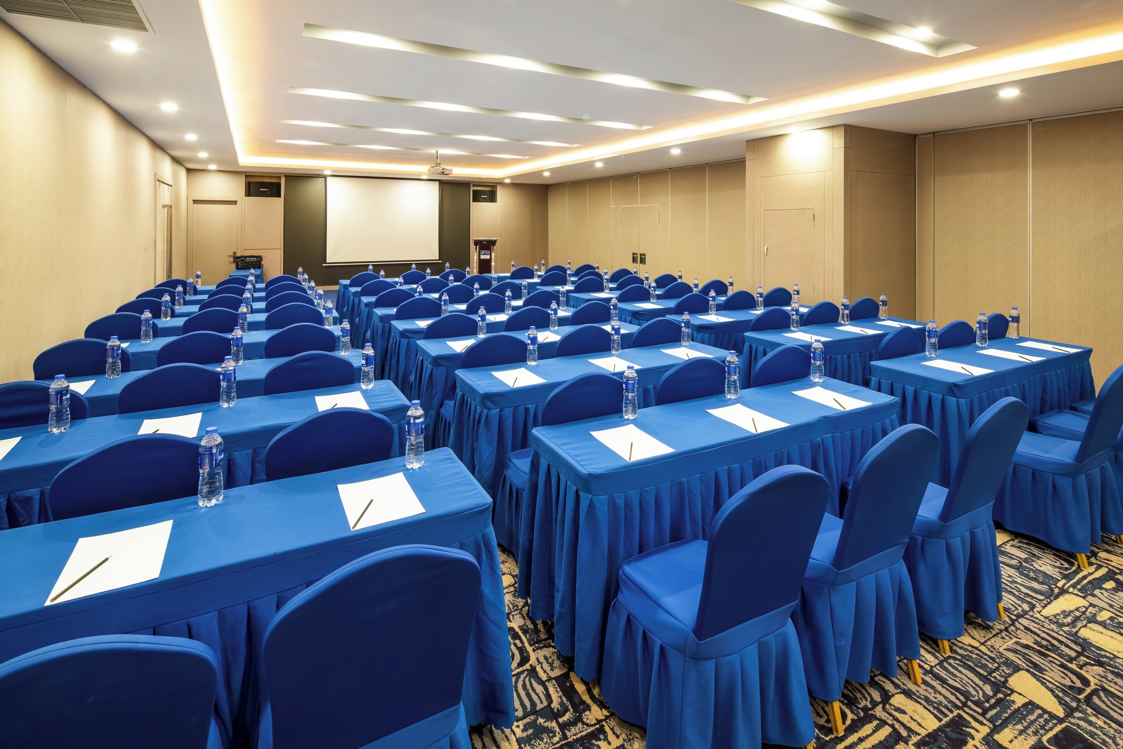Un salón de conferencias con filas de mesas y sillas, equipado con botellas de agua y tarjetas de identificación.