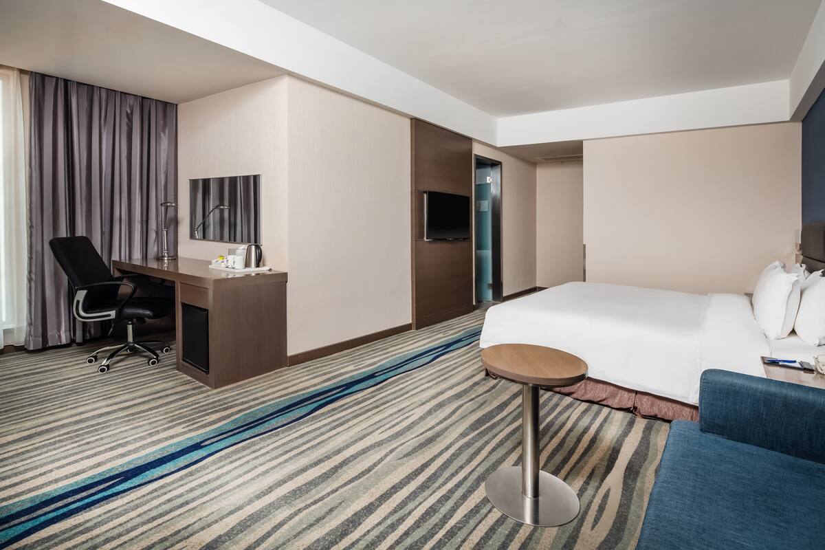 A hotel room with a bed, a desk with a chair, a TV, and a small round table.