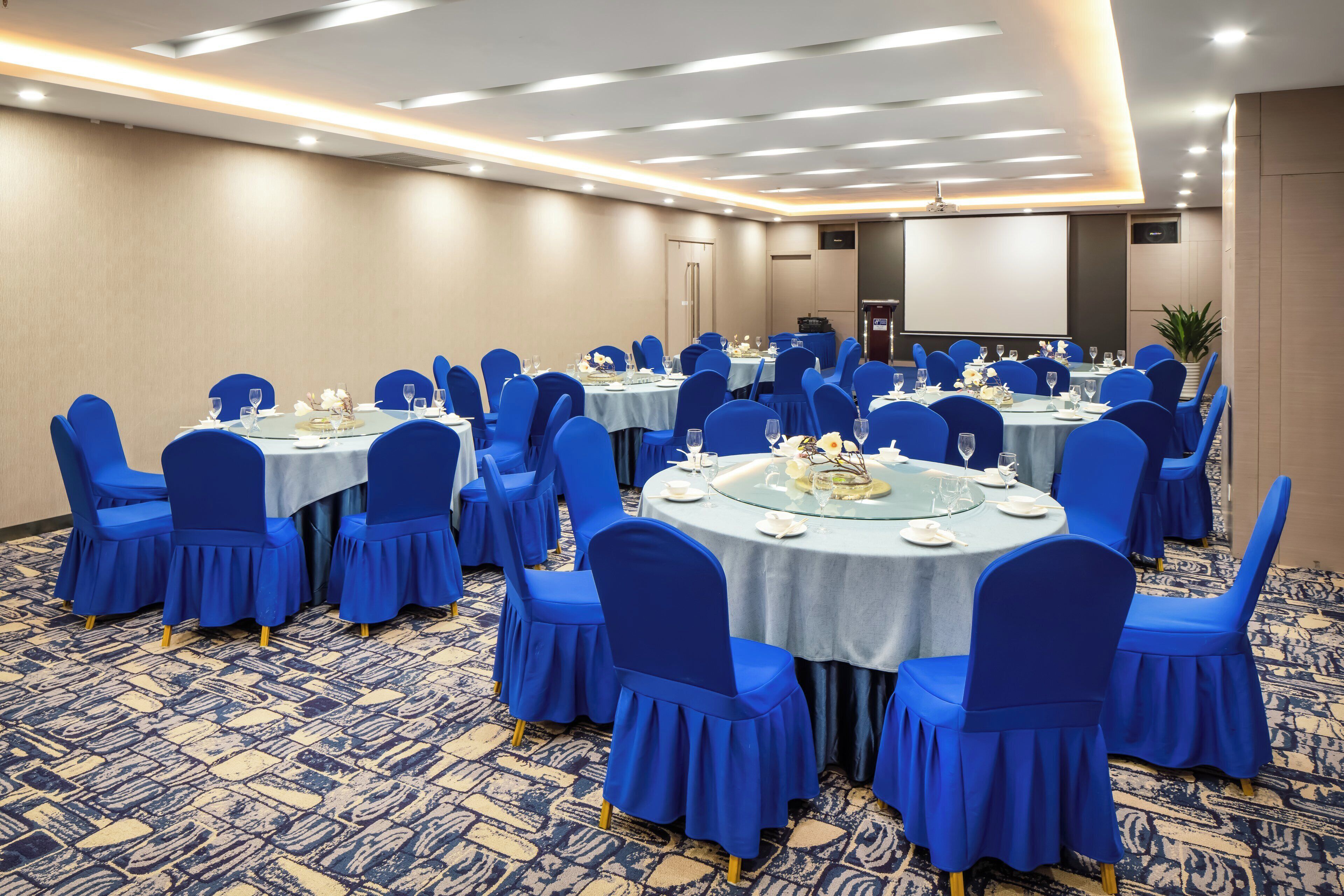 A conference room with round tables, blue chairs, and a projector screen.