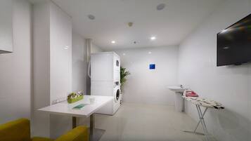 A compact hotel room with a washing machine, a sink, a television, and a small table with a chair.