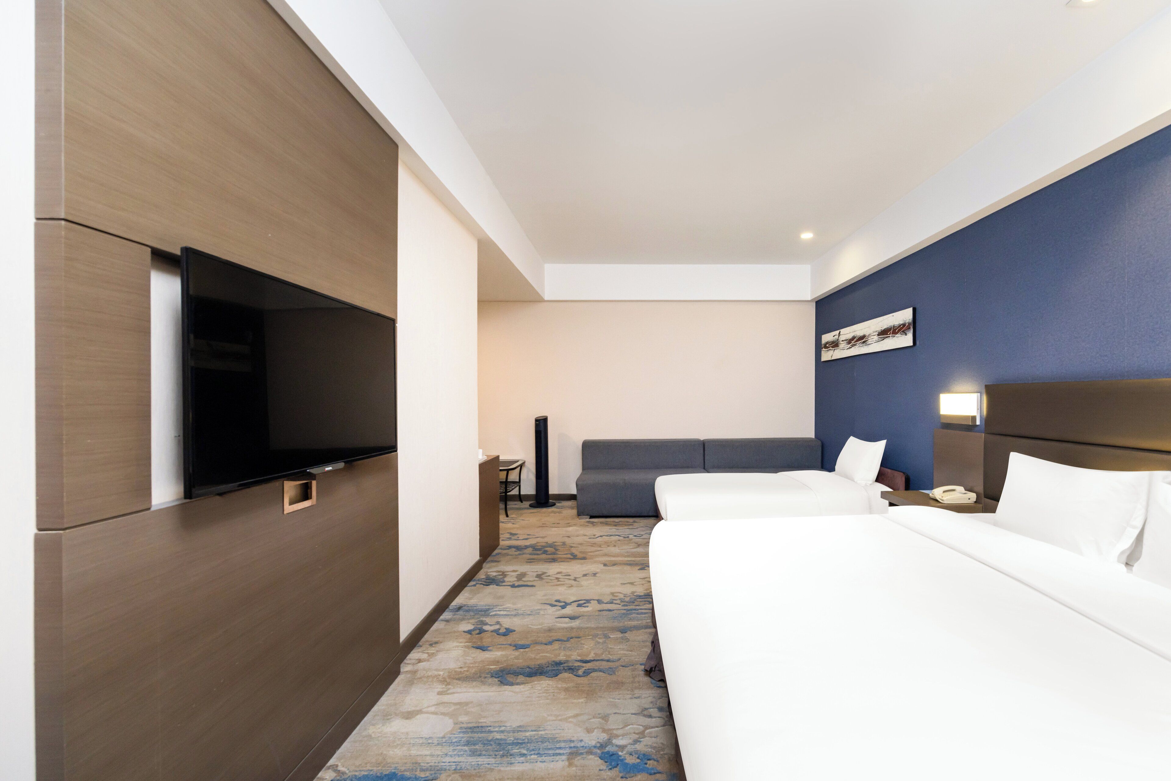 A hotel room with a flat-screen TV, two beds, a sofa, a desk, and a telephone.