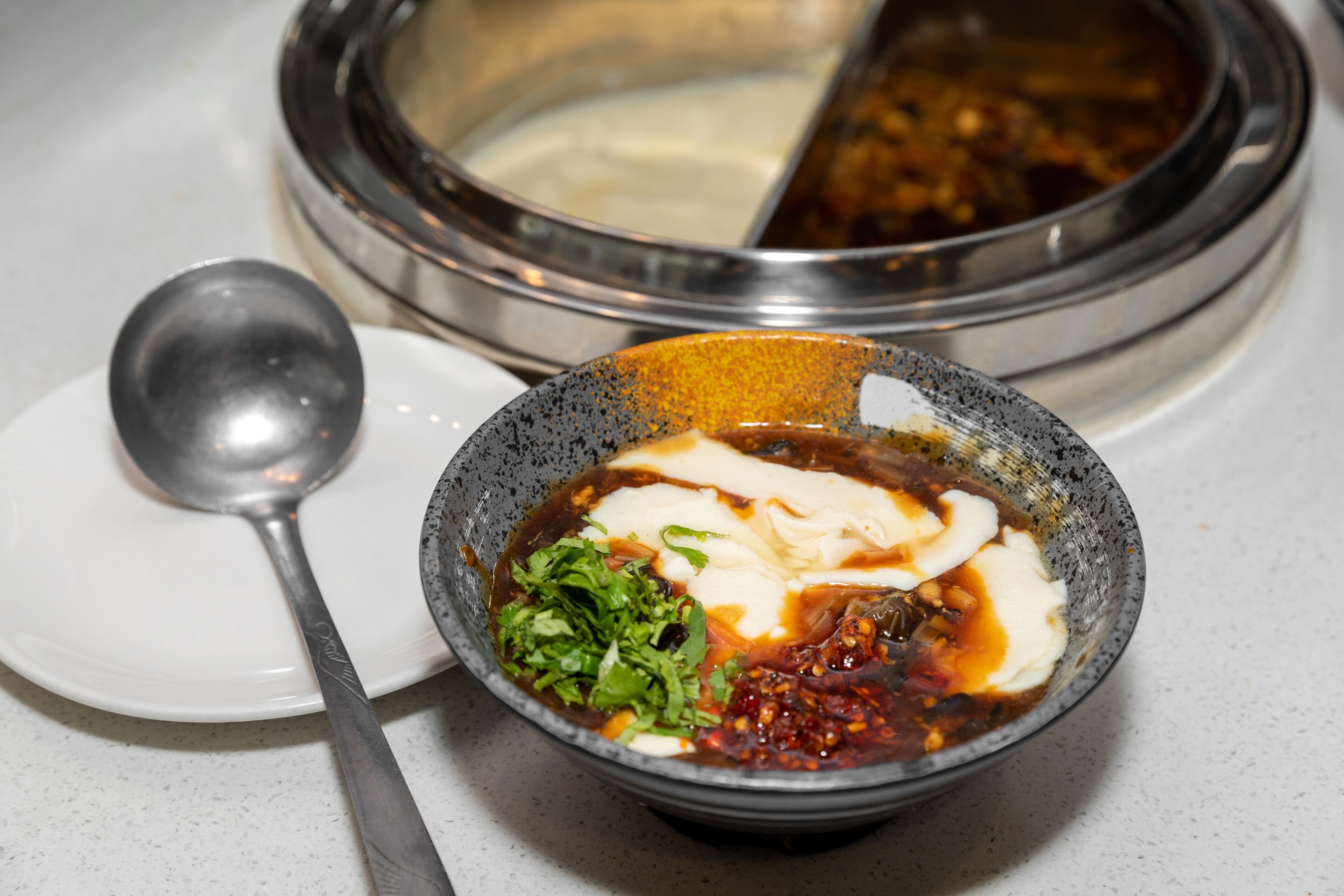 A bowl of soup with various ingredients, a spoon, and a plate.