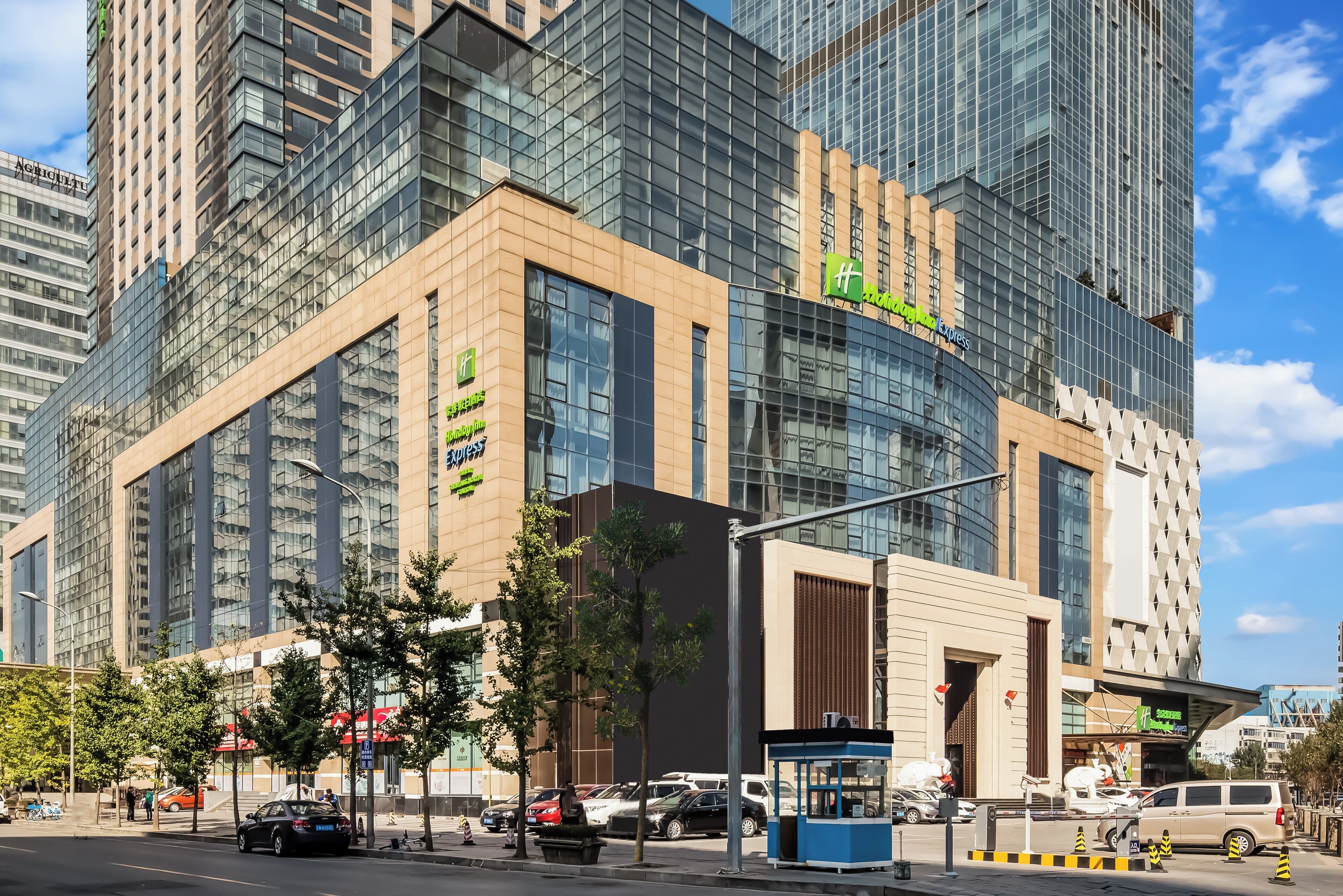 A modern hotel with a glass facade, multiple floors, and a prominent green sign.