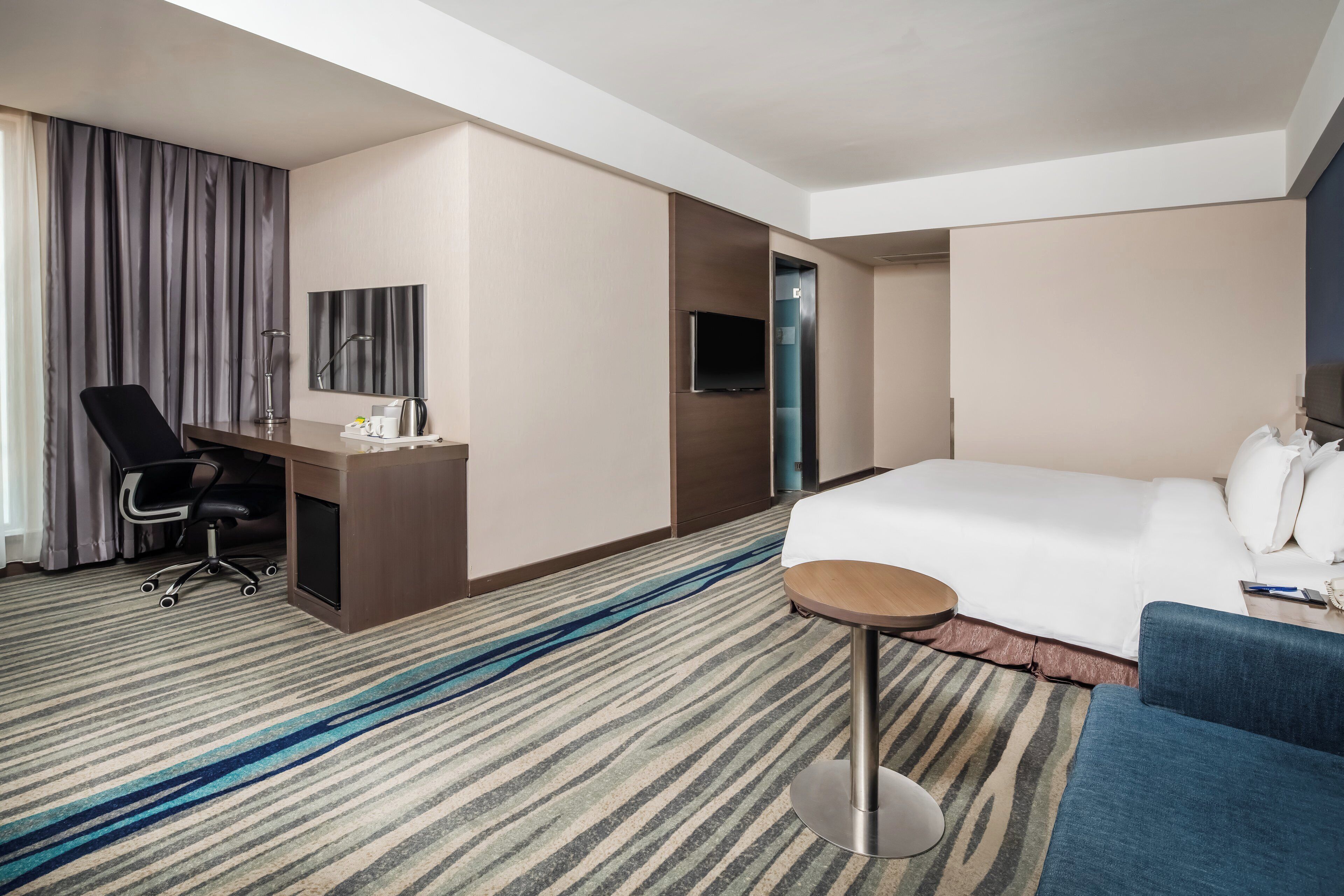 Ein Hotelzimmer mit Bett, Schreibtisch mit Stuhl, Fernseher und einem kleinen runden Tisch.