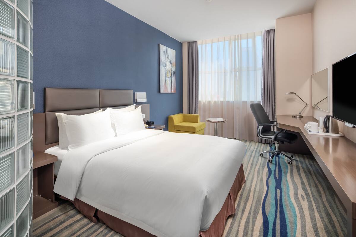 A hotel room with a large bed, a desk with a chair, a TV, and a window with curtains.
