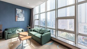 A modern hotel room with a large window, a green sofa, a small table, and a painting on the wall. - Holiday Inn Express Shenyang North Station by IHG (Shenyang)