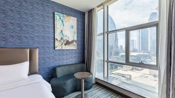 Une chambre d’hôtel avec une grande fenêtre, un lit, un canapé bleu et une petite table.