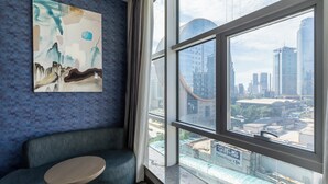 A modern hotel room with a large window offering a city view, a comfortable seating area, and a large abstract painting on the wall. - Holiday Inn Express Shenyang North Station by IHG (Shenyang)