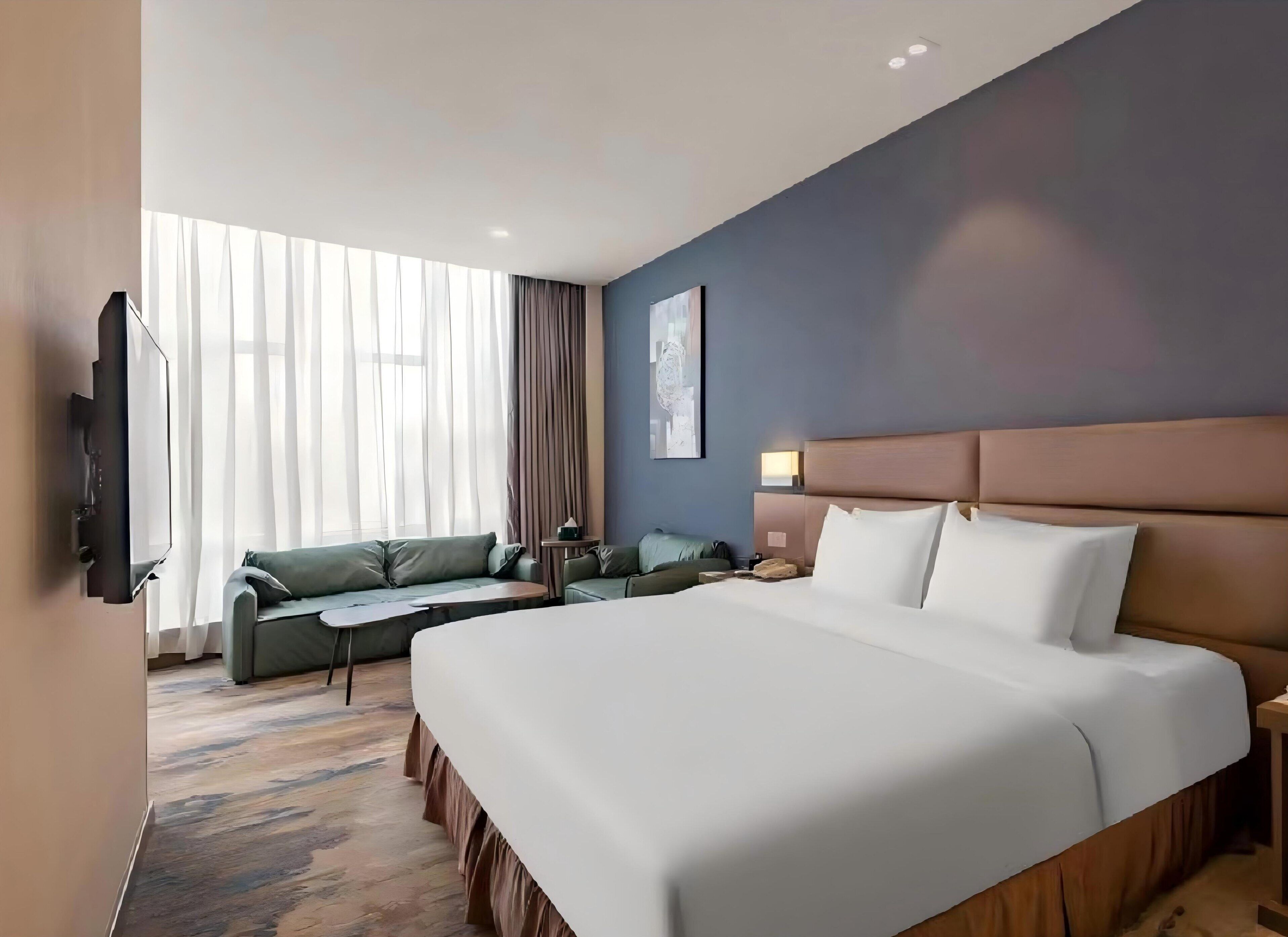 Habitación de hotel con una cama grande, un sofá, una mesita y un televisor.
