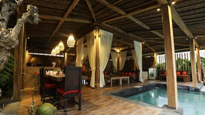 Un área de piscina con vigas de madera, una zona de comedor con sillas rojas y un bar con mostrador.