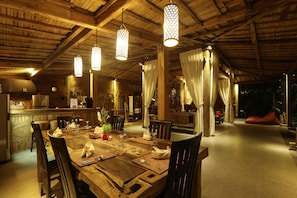 A wooden dining area with a long table set for a meal, surrounded by chairs.