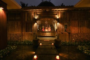 A traditional wooden structure with a central altar, surrounded by a wooden fence and a pathway with candles.