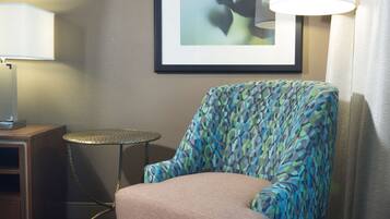 A room with a patterned armchair, a framed abstract painting, a small round table, and a lamp.