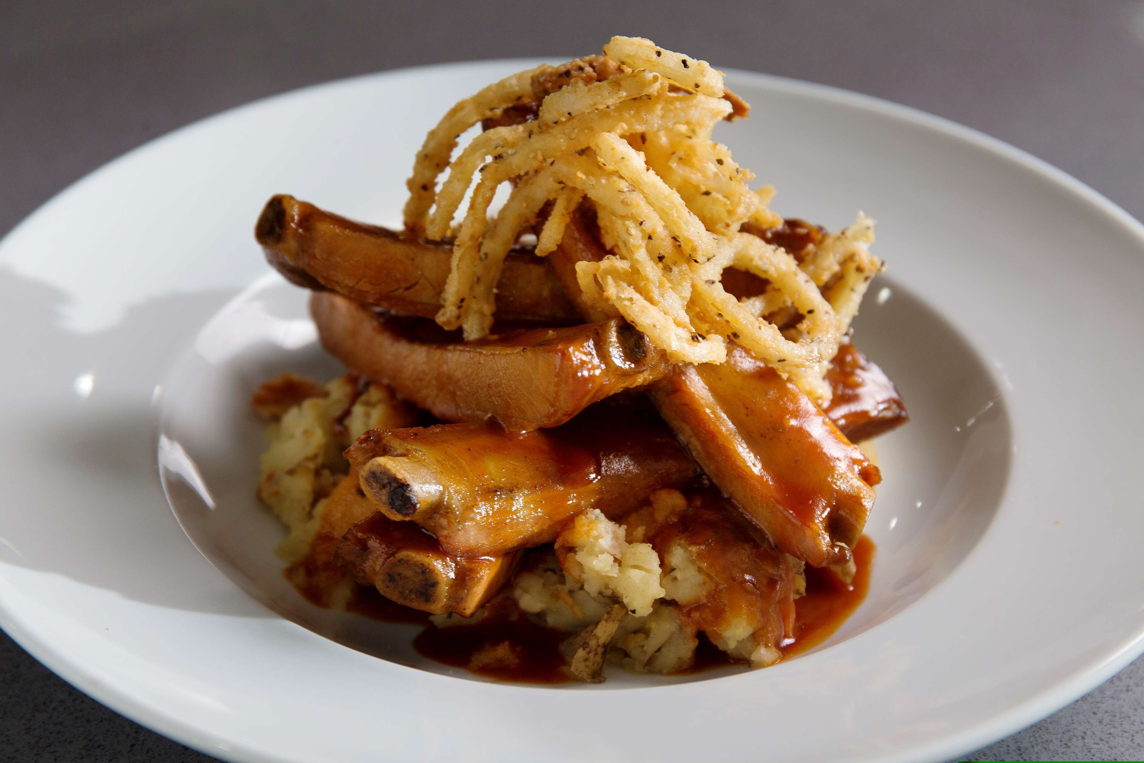 Une assiette de nourriture comprenant des travers de porc, de la purée de pommes de terre et des oignons frits.