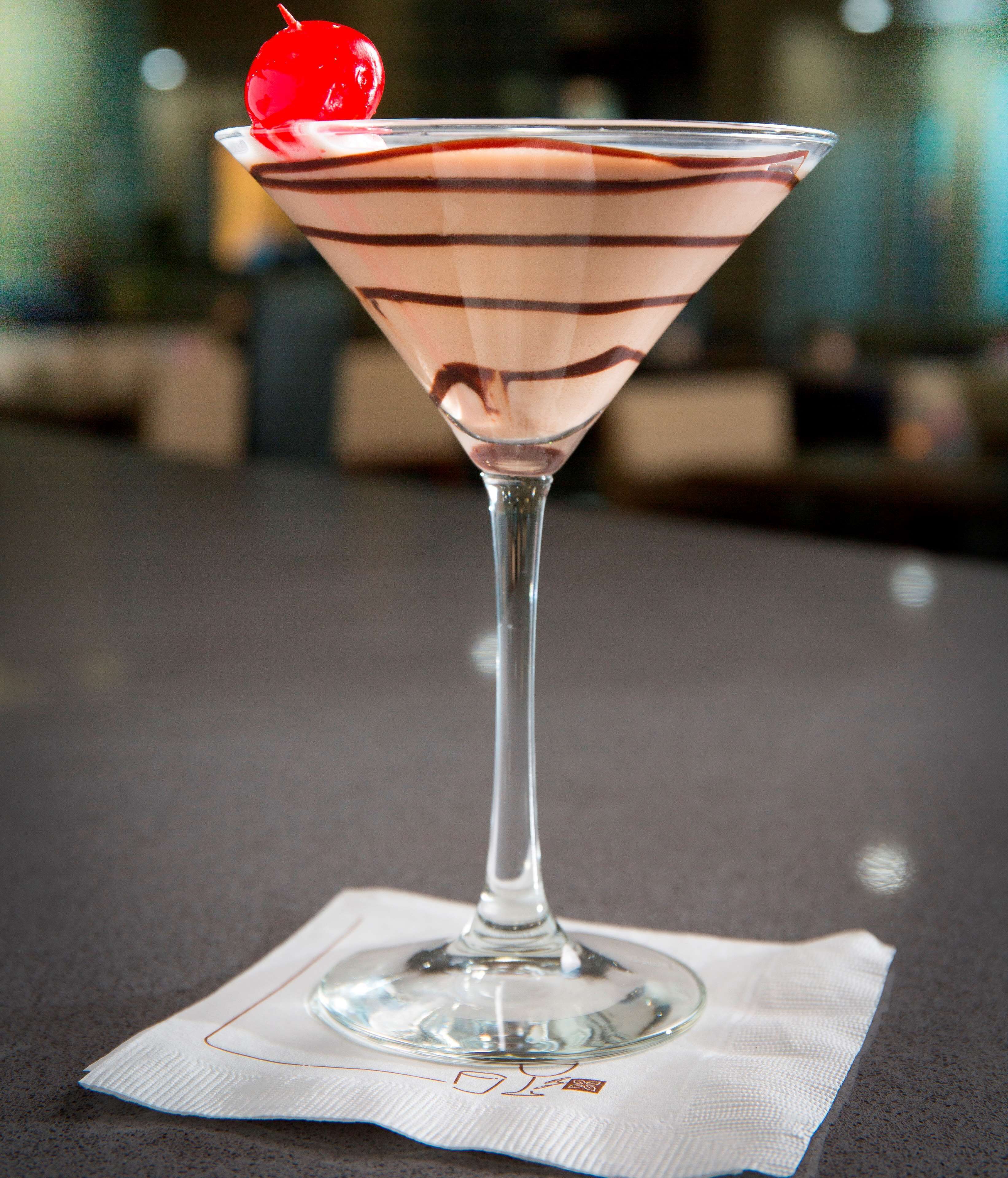A martini glass with a cherry on the rim, placed on a napkin on a table.