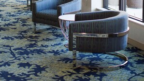A hotel lobby with a patterned carpet, curved seating, a small table, and a vase of flowers. - Hilton Garden Inn Longview (Longview)
