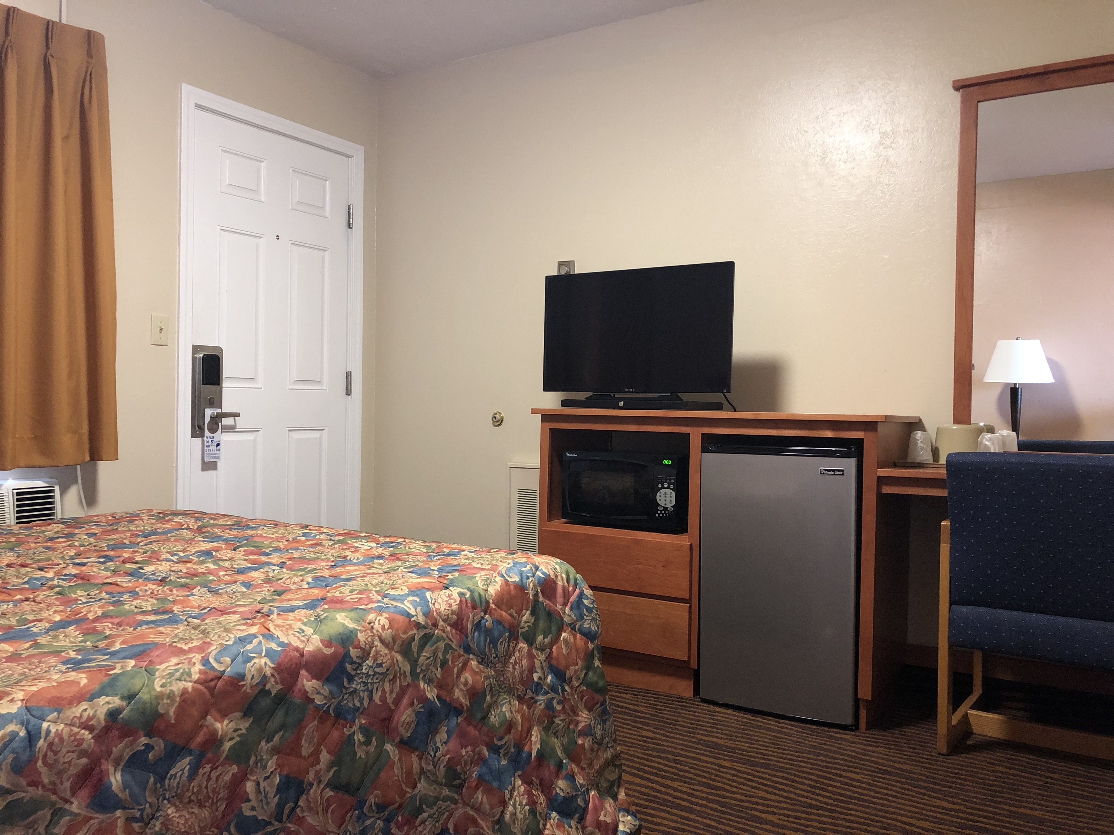 Une chambre d’hôtel équipée d’un lit, d’un bureau avec une télévision, d’un four à micro-ondes et d’un réfrigérateur.