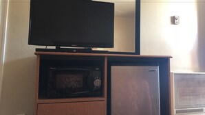 A television on a wooden stand, a microwave, and a refrigerator in a room with a white wall and a ceiling light. - Evergreen Lodge (Mount Shasta)