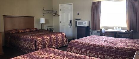 A hotel room with two beds, a desk, a chair, a microwave, and a window with curtains.