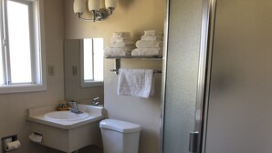 A bathroom with a toilet, sink, and shower. There are towels stacked on a shelf and a mirror above the sink. - Evergreen Lodge (Mount Shasta)