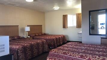 Habitación de hotel con dos camas, una mesita de noche con lámpara, un espejo y una ventana con cortinas.