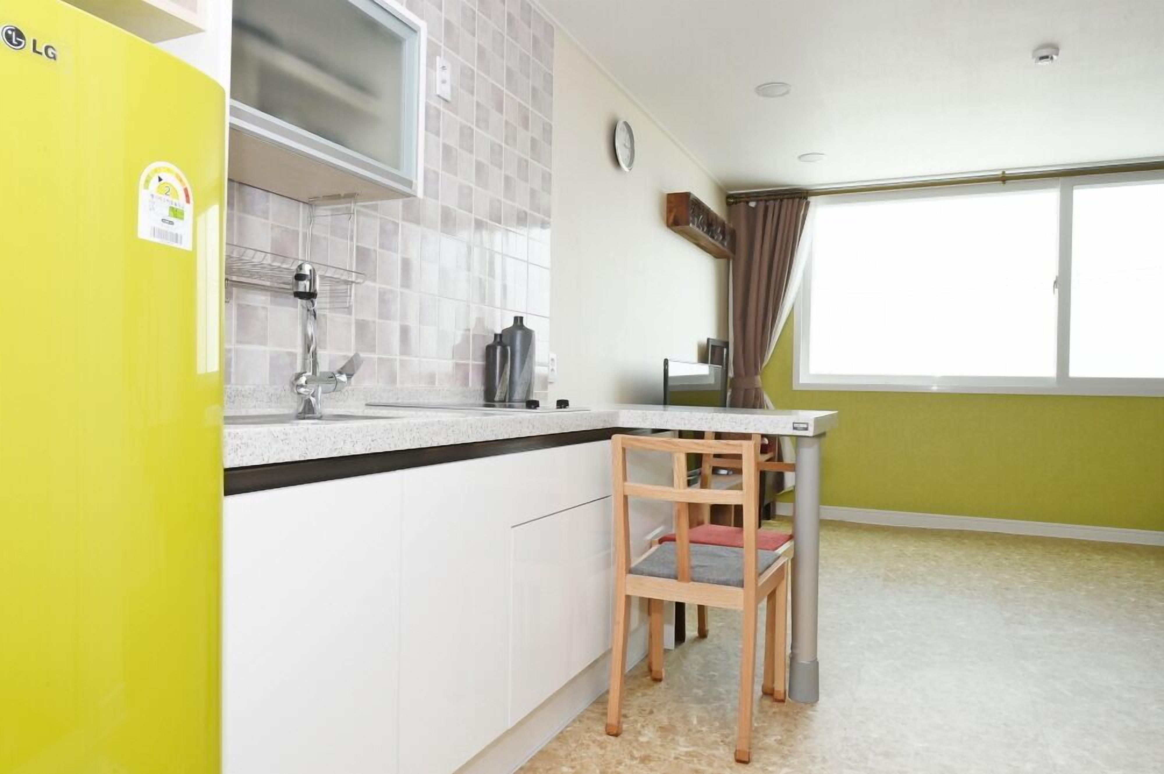 Una cocina compacta con un refrigerador amarillo, un lavamanos y una ventana con cortinas.