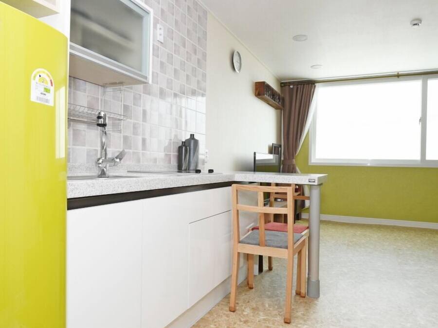 Una cocina compacta con un refrigerador amarillo, un lavamanos y una ventana con cortinas.