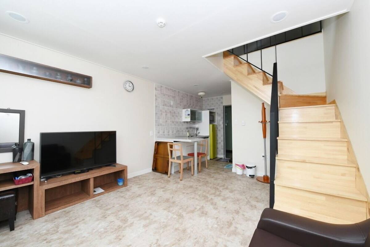 A living room with a TV, wooden entertainment unit, and a staircase leading to a kitchen.