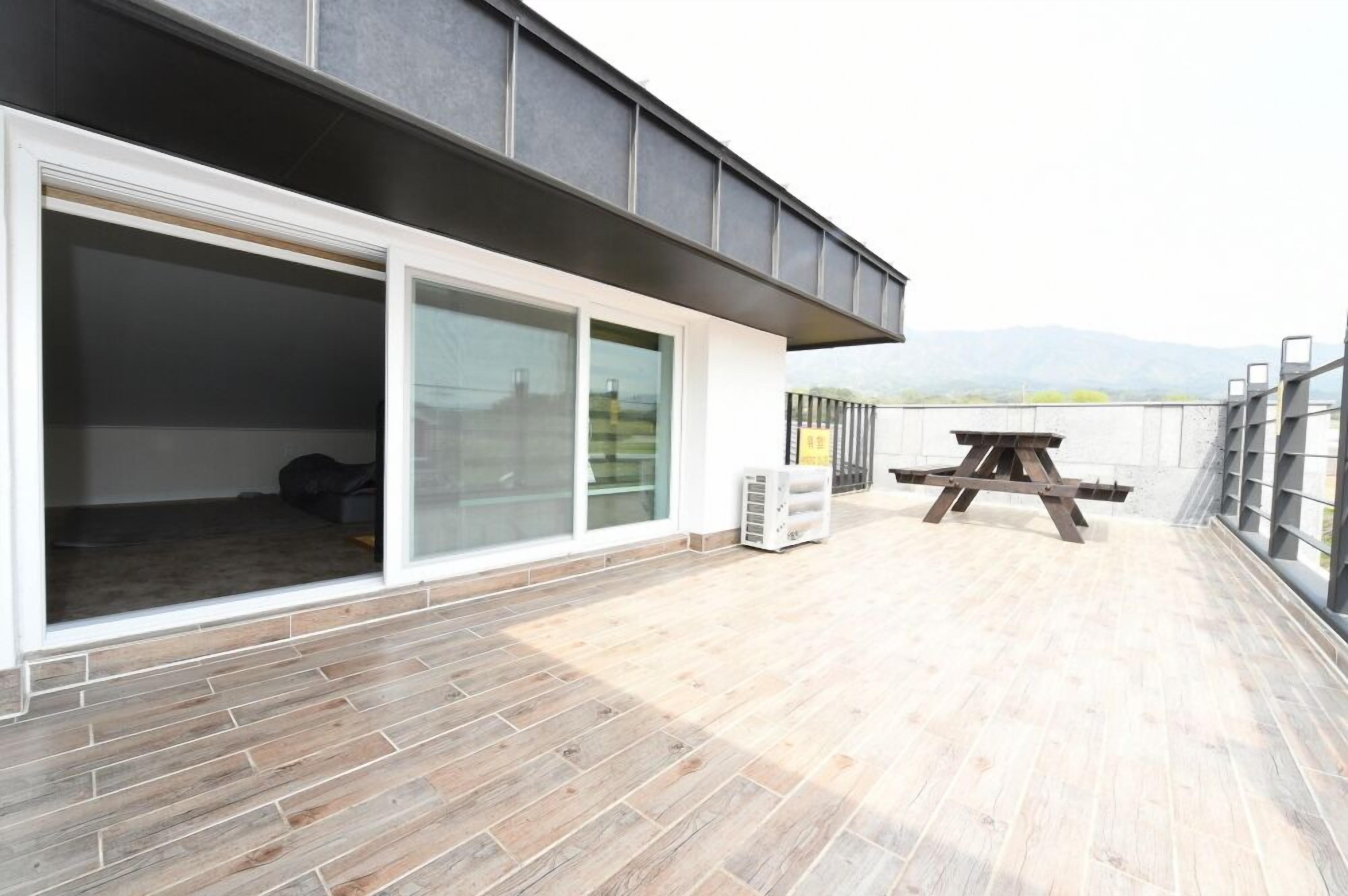 Un espacio de sala-comedor abierto con un ventanal corredera que da a un balcón, una mesa de madera y un equipo de aire acondicionado blanco.