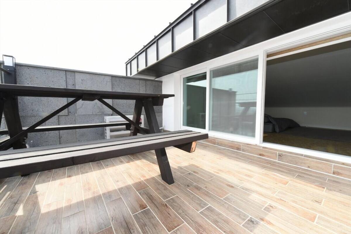 An outdoor patio with a wooden table and benches, a concrete wall, and a sliding glass door leading to an interior space.
