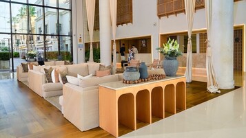 A spacious lobby with a modern sofa arrangement, a wooden console table with decorative vases, and large windows offering views of the surrounding buildings.