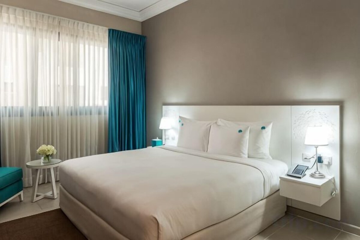 A hotel room with a large bed, a bedside table with a lamp, and a small table with a vase of flowers.