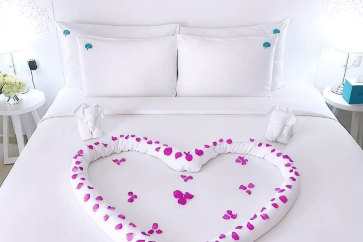 A bed with a heart-shaped arrangement of rose petals and a white towel.