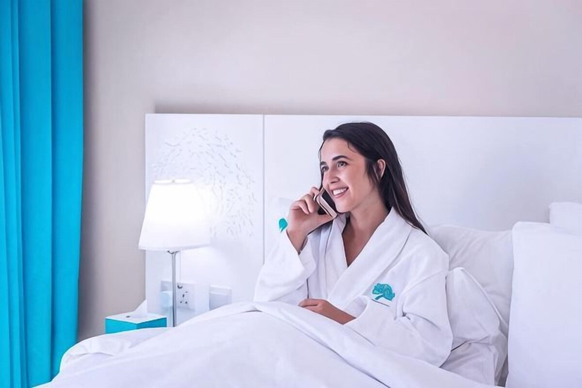 A hotel room with a bed, a nightstand, a lamp, and a wall with a textured design.