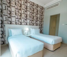Habitación de hotel con dos camas, pared con estampado de piedra, una mesita con lámpara y una puerta.