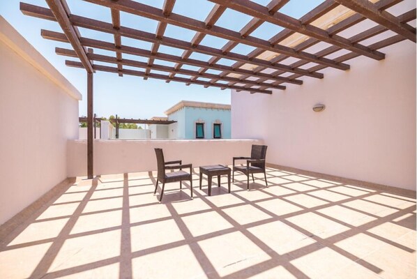 Un patio exterior con pérgola, dos sillas y una pequeña mesa.