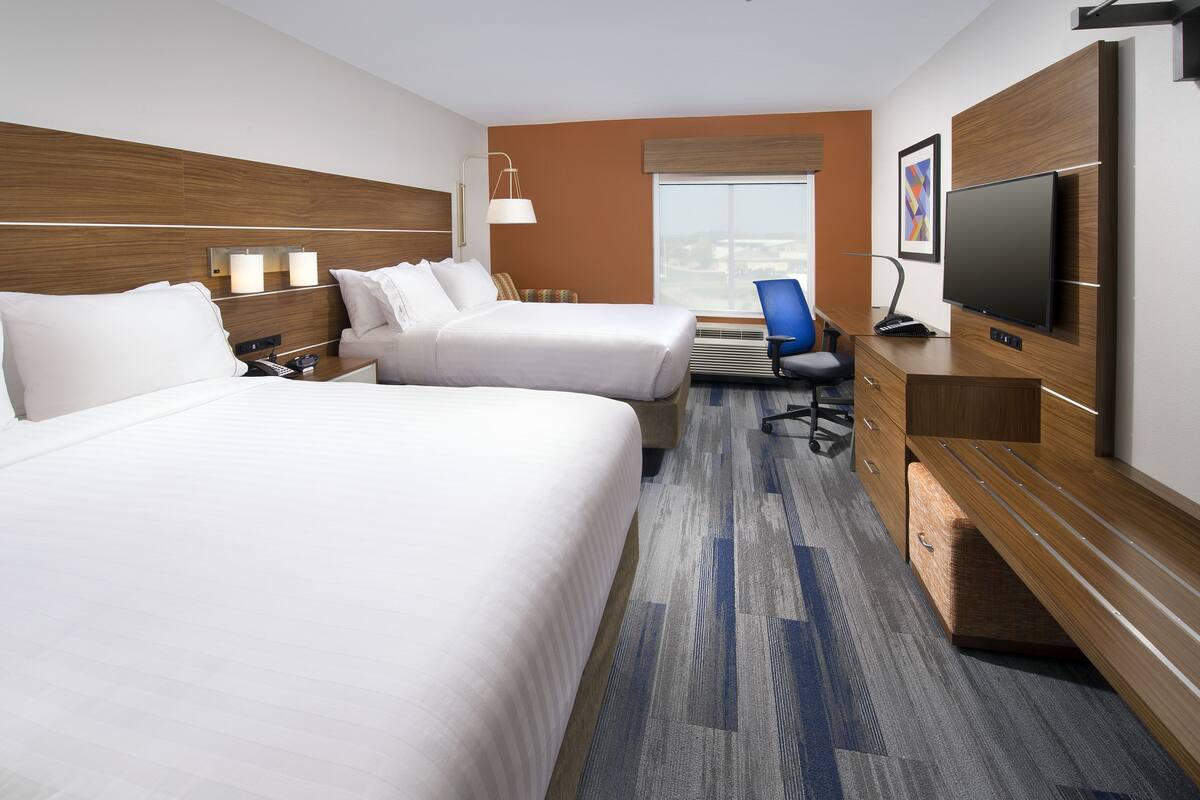 A hotel room with two beds, a desk, a chair, a TV, and a window with a view.