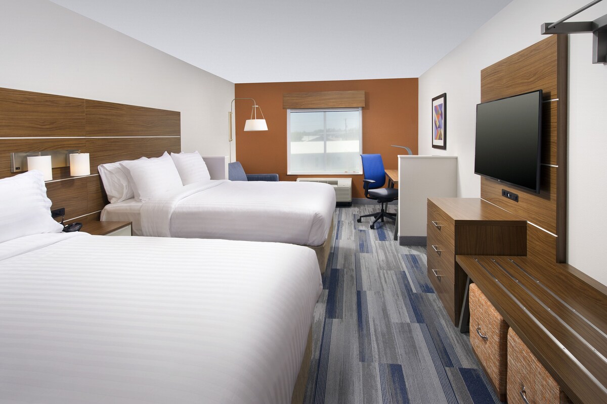 A hotel room with two beds, a desk, a chair, a TV, and a window.