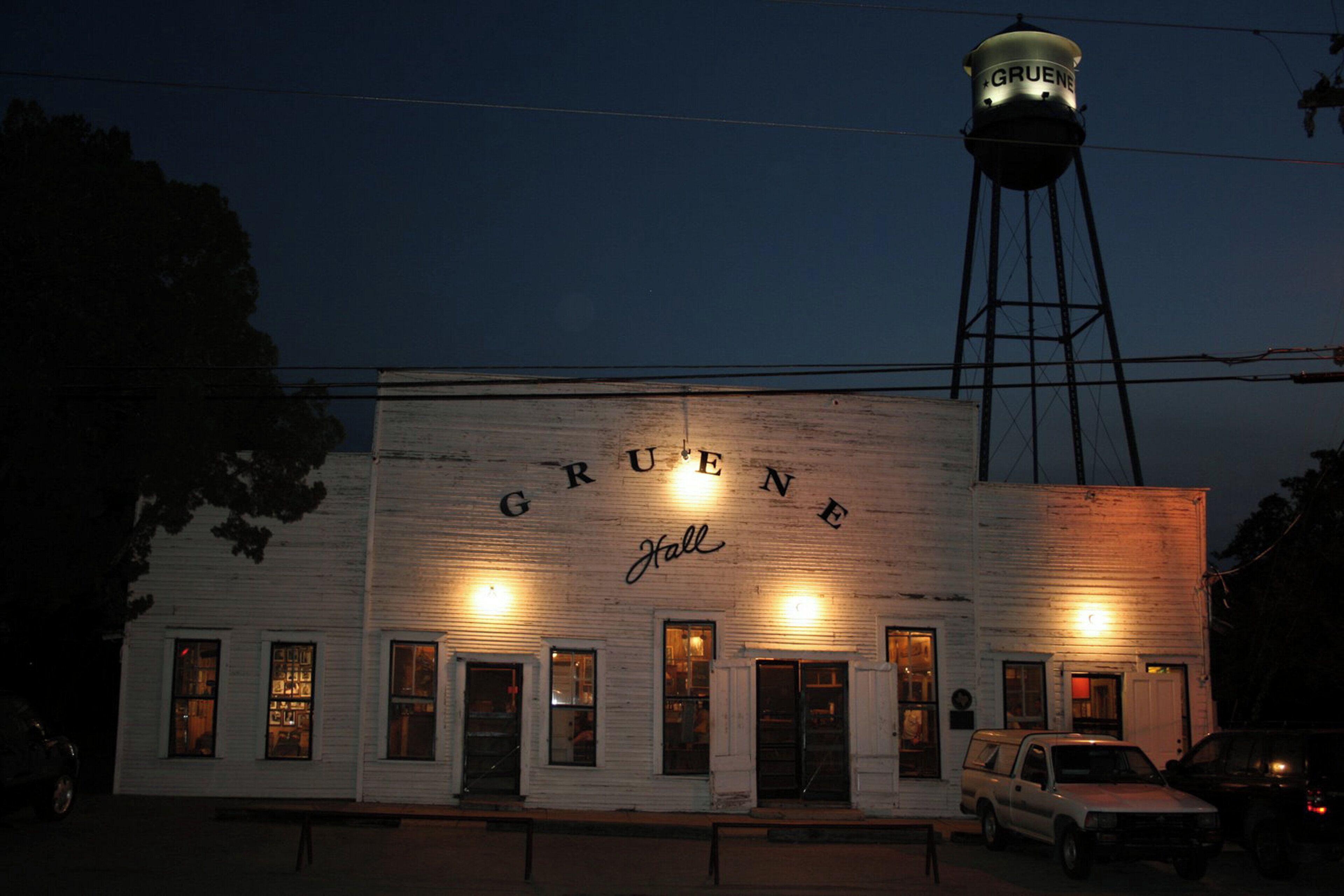 A building with 'GRUENE Hall' written on the facade, a water tower in the background, and a parked vehicle in front.