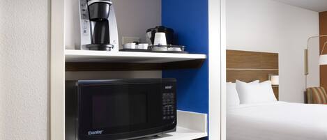 A hotel room with a microwave, coffee maker, and a compact refrigerator on a white shelf.