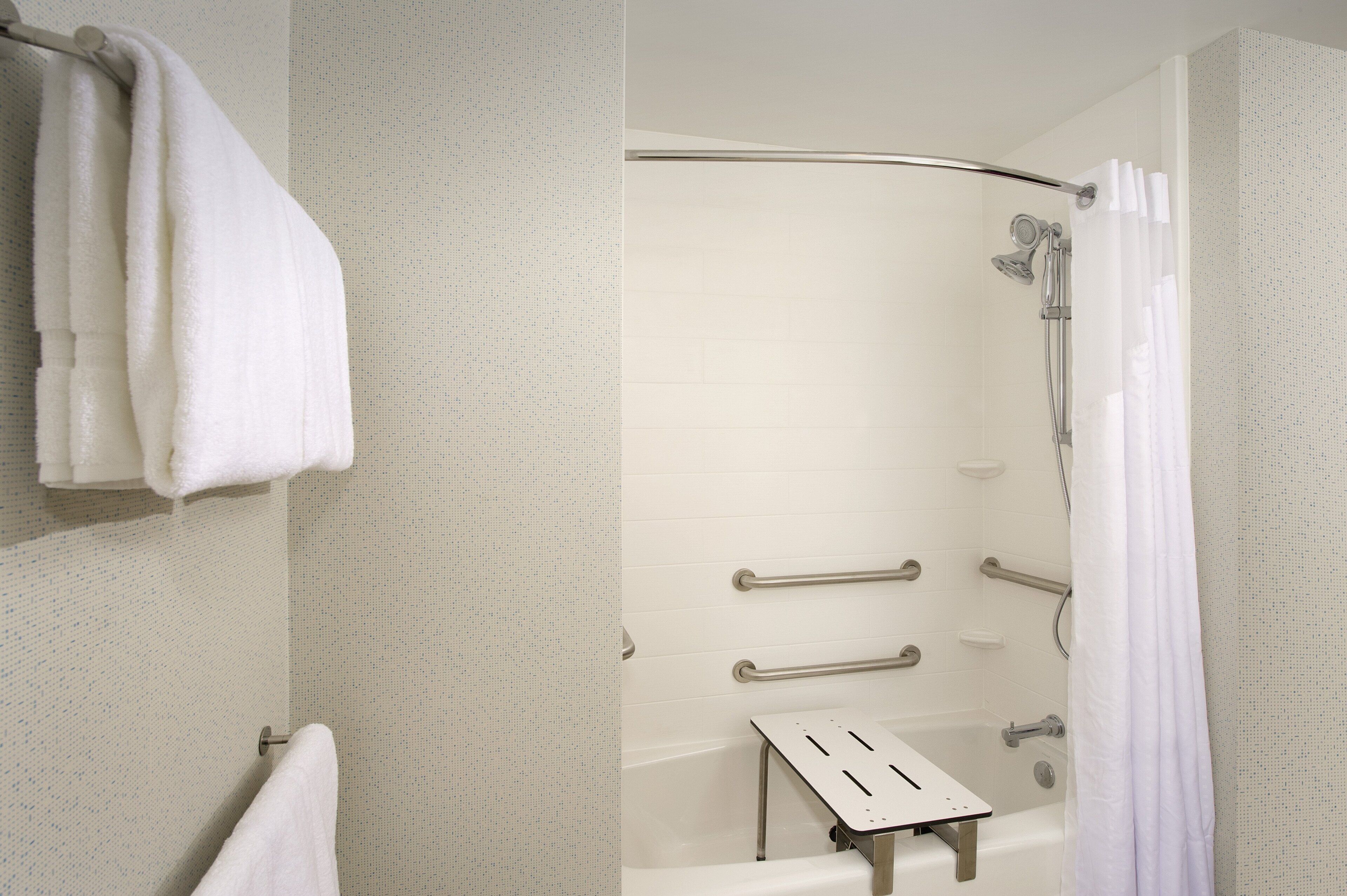 Un baño moderno con ducha, barras de apoyo y un perchero para toallas.