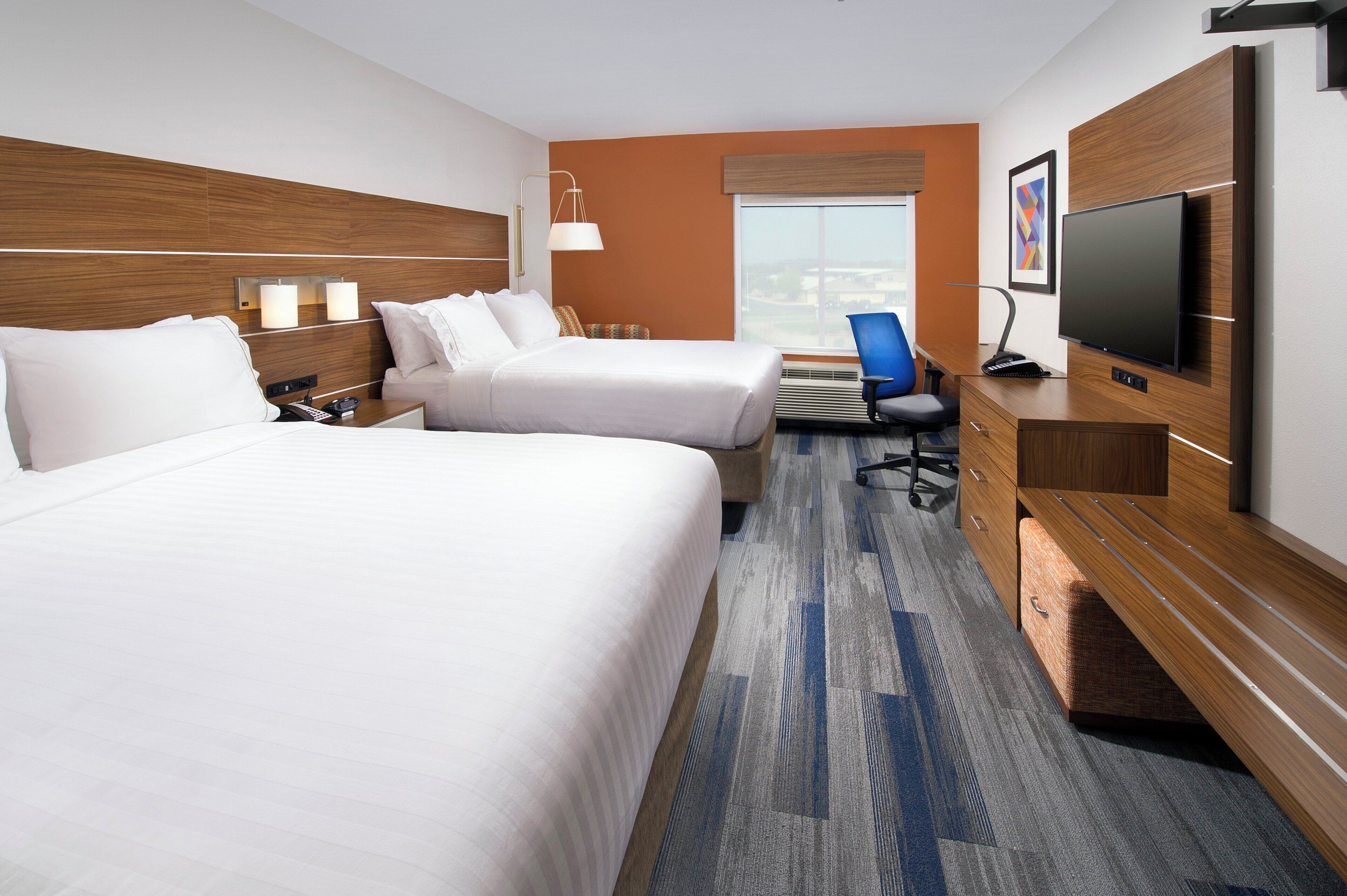 A hotel room with two beds, a desk, a television, and a window with a view.