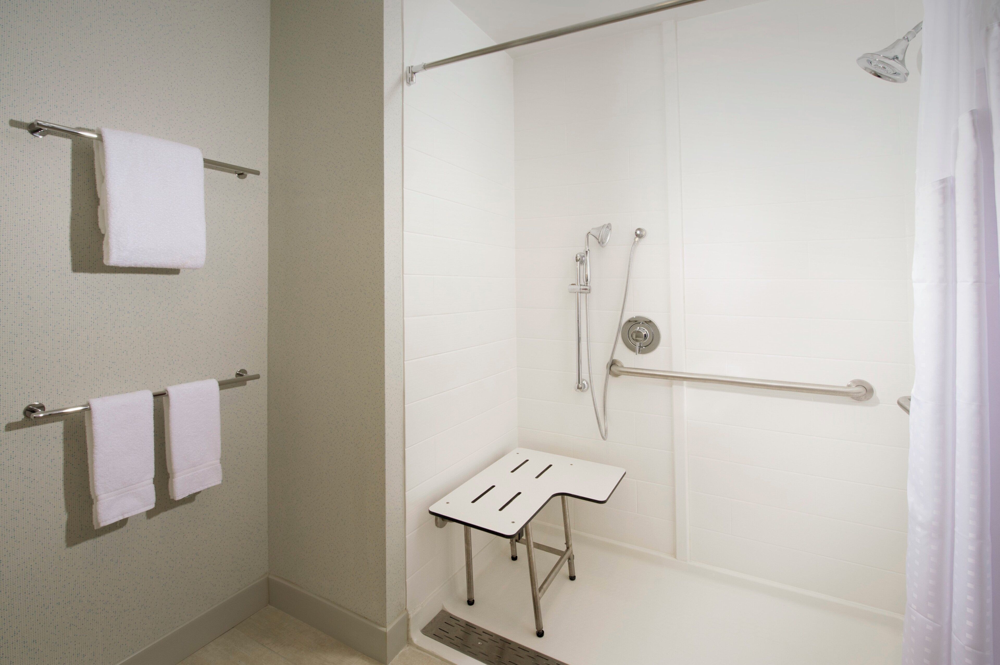 A bathroom with a shower, a towel rack, and a small table.