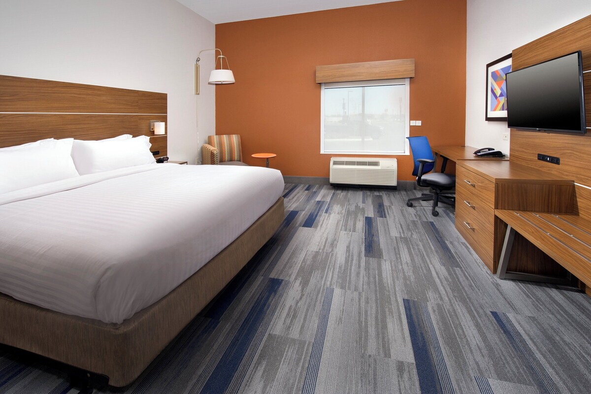A hotel room with a large bed, a desk with a chair, a television, and a window with blinds.