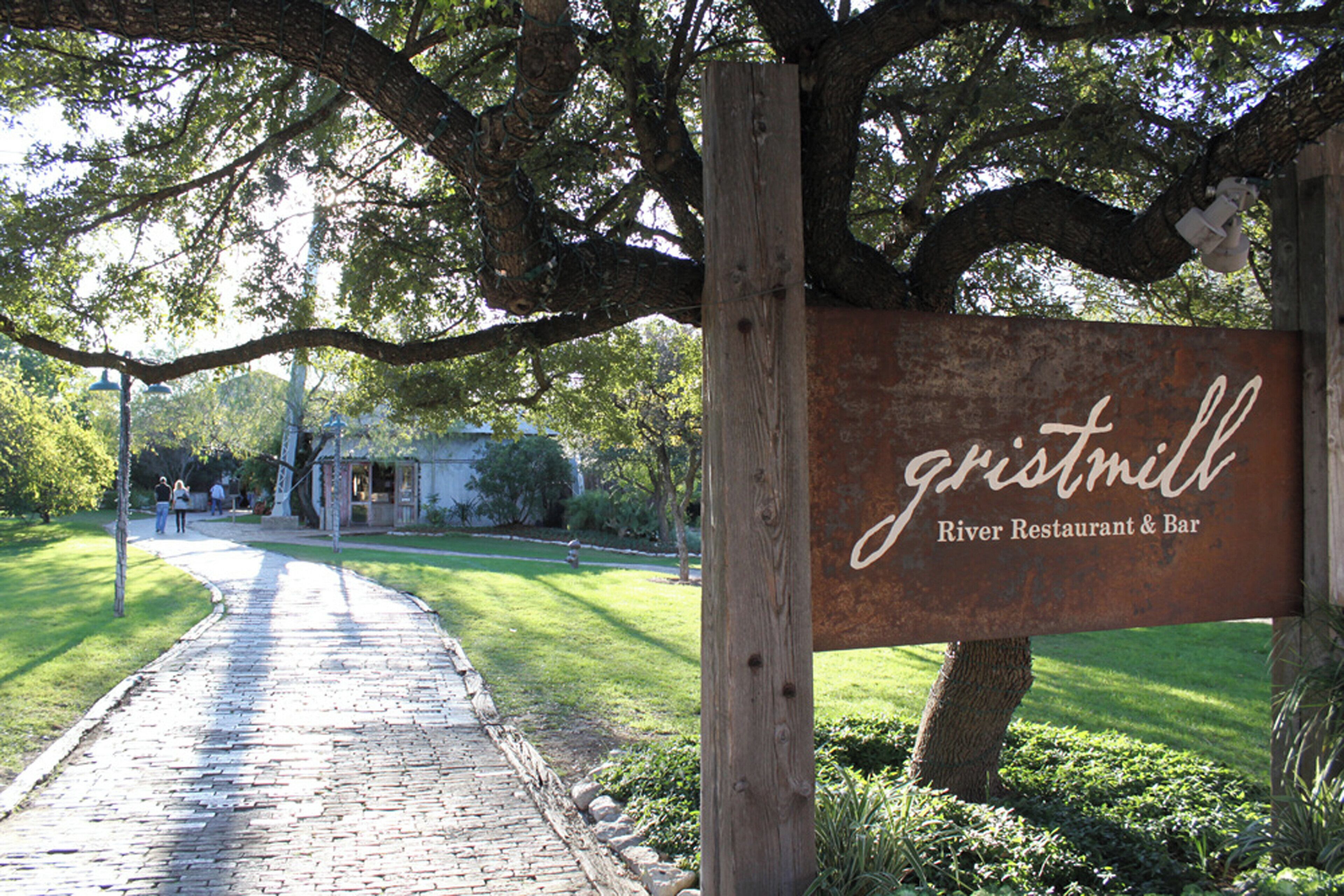 A rustic wooden sign for a restaurant and bar named 'gristmill' with a paved pathway leading to it.