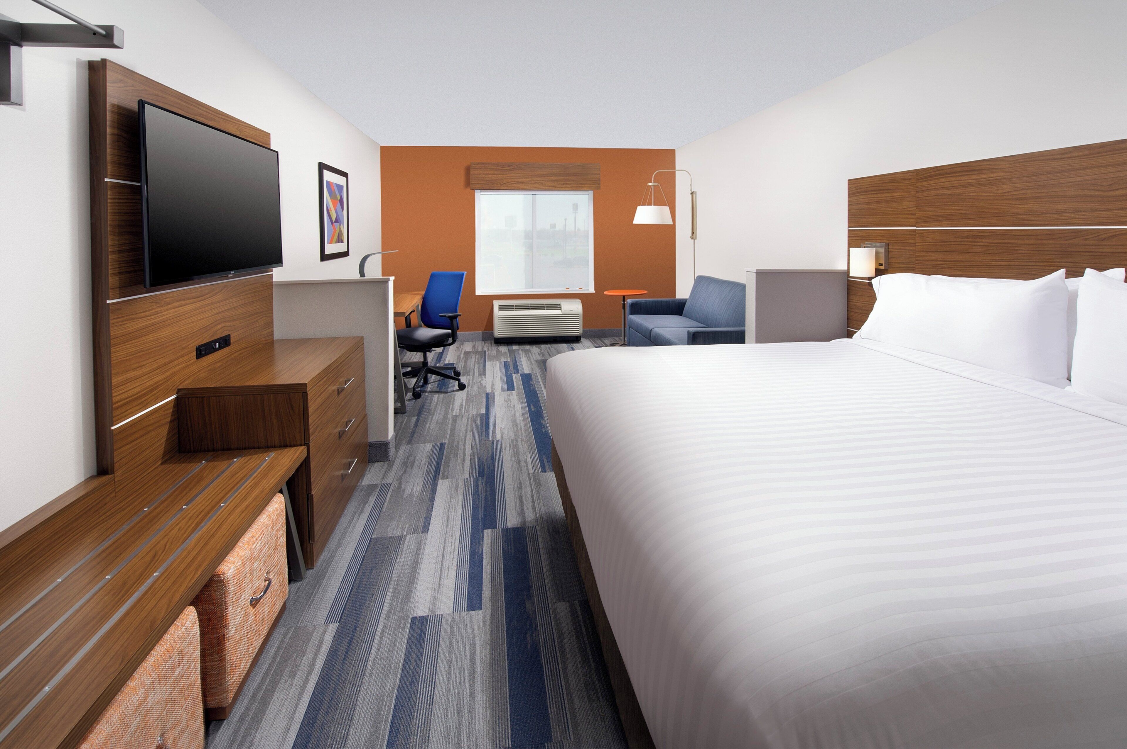 Une chambre d’hôtel comprenant un lit, un bureau avec un téléviseur à écran plat, une chaise, un canapé et une fenêtre donnant sur un paysage agréable.